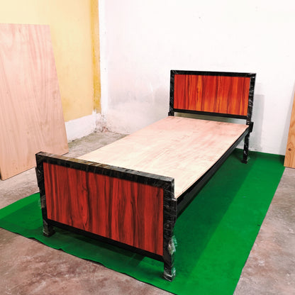 Wooden bed frame with red and black design on a green mat against a plain wall.